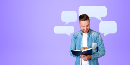 Portrait of cheerful young man college student writing in notebook standing over purple background...
