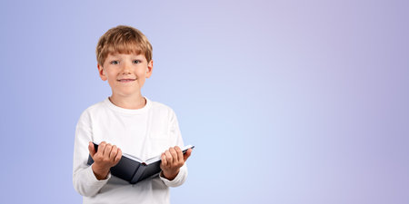 Happy school boy standing with book in hands, front portrait on empty copy space purple background....