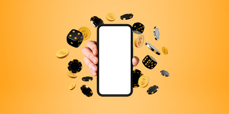 Hand of man holding smartphone with mock up screen and dice, poker chips and dollar coins over yellow background. Concept of online casino and successの写真素材
