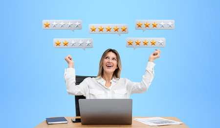 Smiling office woman with raised hands, workplace with laptop. Looking up at low or high rating online, speech bubbles with stars. Concept of customer feedback and business serviceの写真素材
