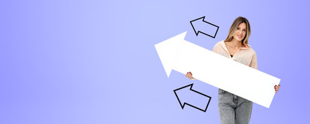 Portrait of cheerful young European businesswoman holding mock up arrow standing over purple copy space background with two arrows drawn on it. Concept of product and services advertisingの写真素材