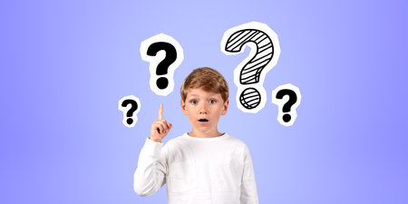 Surprised school boy with finger pointing up, amazed portrait with opened mouth. Question marks doodle on bright background. Concept of problem and solutionの写真素材