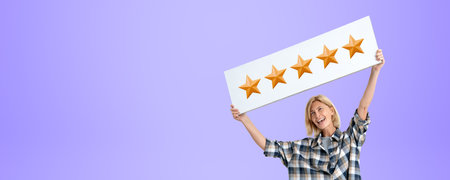 Smiling young woman holding up a signboard with five gold stars, empty copy space purple background. Concept excellent service, evaluation and customer feedbackの写真素材