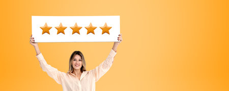 Smiling young woman holding up a white signboard with five gold stars, empty orange background....