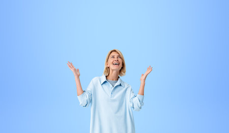 Portrait of cheerful young European woman wearing casual clothes and celebrating victory with raised...