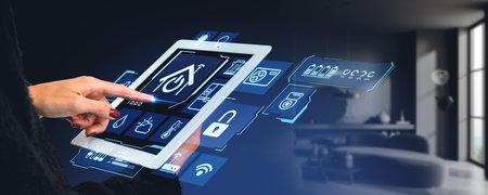 Hands of woman holding tablet computer with smart home app in blurry living room. Concept of IoT...