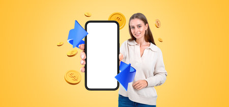 Smiling woman showing mockup smartphone display, blue arrow with coins falling on yellow background....