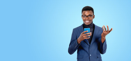 Happy black businessman using phone, making a friendly hand gesture. Copy space blue background....