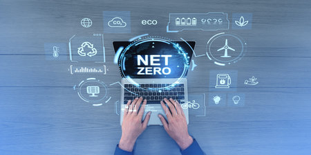 Hands typing on a laptop displaying NET ZERO surrounded by eco-friendly icons like recycling, wind turbine, and plant on a wooden background. Concept of sustainable energy and ecologyの写真素材