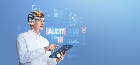 Man in white shirt using a tablet with digital audit graphics overlay on a blue background. Concept of technology in auditingの写真素材