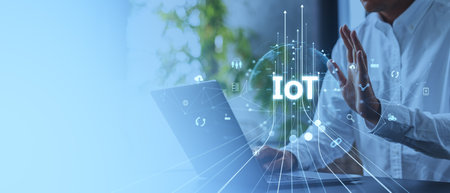 Image of a person interacting with IoT digital icons above a laptop. Blue-toned background with...