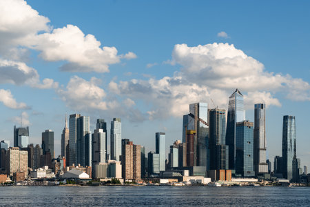 New York City skyline featuring tall skyscrapers and modern buildings along the waterfront. Clear blue sky with scattered clouds. Concept of urban cityscapeの写真素材