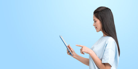 Profile of smiling Asian woman finger touch tablet display, copy space empty blue background....