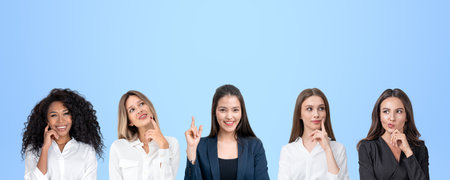 Thoughtful portraits of multinational businesswomen in row, smiling and finger pointing up portraits on copy space blue background. Concept of startup idea, teamwork and conferenceの写真素材