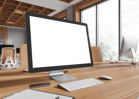 A desktop computer with a blank screen on a wooden desk, placed in a modern office with large windows and natural light. 3D Renderingの写真素材