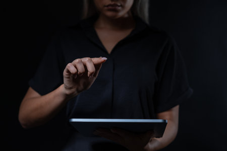 Woman interacting with a digital tablet, focus on hands, against dark background. Concept of technology and gadget useの写真素材