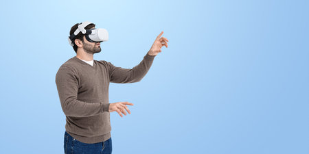 Excited young man in vr glasses headset, finger touching something on blue empty copy space...