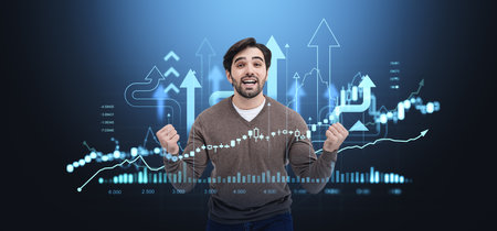 Happy man holding fists, forex hologram with lines, growing arrows and candlesticks, stock market dynamics. Concept of investment, business success and profitの写真素材