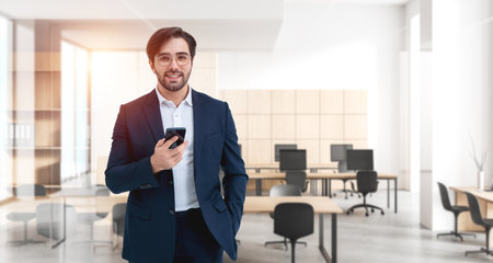 Smiling businessman using smartphone, coworking room interior and meeting space. Concept of business connection, online network and virtual meetingの写真素材