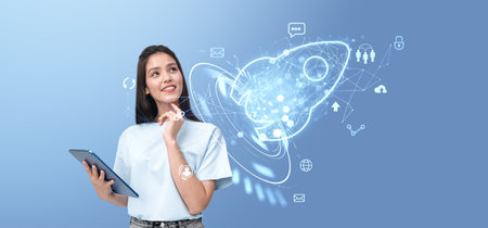Dreaming woman holding tablet, glowing rocket with diverse business and marketing icons. Concept of project, social media, connection, technology and innovationの写真素材