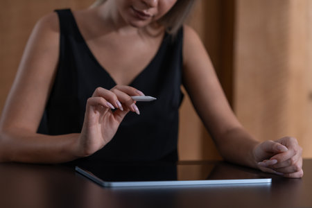Woman hand with pen stylus point at something in the air, digital tablet on desk. Click on a virtual screen. Choice of products or services. Concept of technology, internet and work processの写真素材