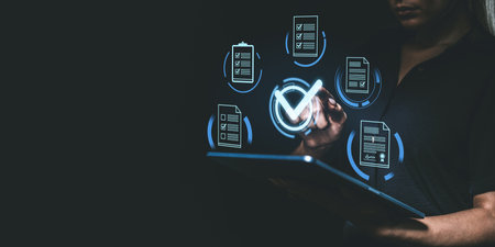 Person using a tablet with digital checkboxes and documents on a dark background, symbolizing project management and quality approvalの写真素材