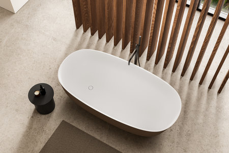 Top view of cozy hotel bathroom interior with white bathtub and side table, wooden slats and concrete floor. Bathing corner in modern apartment with panoramic window. 3D renderingの写真素材