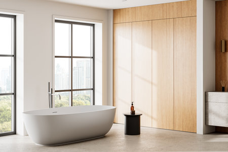 Corner view of home bathroom interior with white bathtub, side table with bathing accessories, wooden shelf on concrete floor. Panoramic window on Bangkok skyscrapers. 3D renderingの写真素材