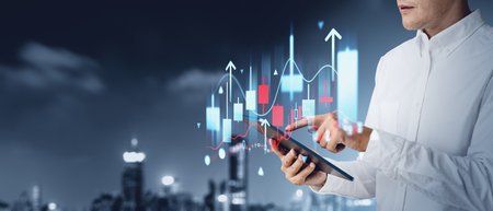 Businessman finger touch tablet in hand, stock market candlesticks and arrows rising. Forex graph analysis and skyline. Concept of online trading, financial idea and investmentの写真素材