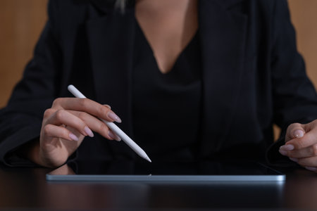 Woman's hands holding a stylus over a digital tablet. Dark background. Concept of modern technology and digital workの写真素材