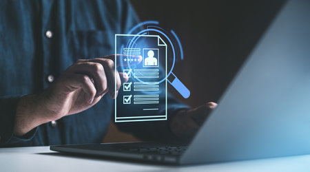 A hand points to a digital resume displayed on a transparent screen while working on a laptop. Dark background. Concept of virtual hiring and recruitmentの写真素材