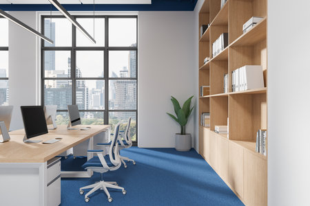 A modern office interior featuring desks, computers, blue carpet, wooden shelving, and large windows with a cityscape background. 3D Renderingの写真素材