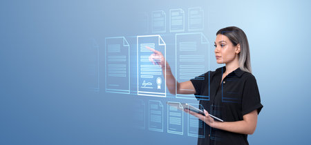 A woman interacts with virtual holographic documents, navigating them with her hand and tablet. Blue digital background. Concept of digital document managementの写真素材