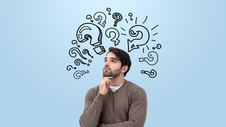 A man deep in thought with his hand on his chin, surrounded by hand-drawn question marks on a light blue background. Concept of ideas and planningの写真素材