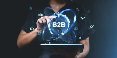 A person uses a tablet displaying glowing B2B icons and digital interface elements on a dark background. Concept of business, technology, and collaborationの写真素材