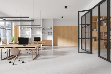 Open office space with wooden walls, desks, computers, and bookshelves, minimalistic design, bright daylight, large windows, coworking concept. 3D Rendering.の写真素材