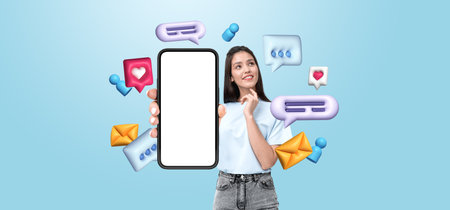 Smiling woman holds phone with blank display, surrounded by vibrant chat bubbles, icons, and envelopes on a light blue backdrop. Communication conceptの写真素材