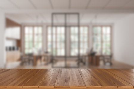 Wooden countertop in focus with blurred modern office interior featuring desks and chairs. Bright natural light through large windows. Concept of presentation. 3D Rendering.の写真素材
