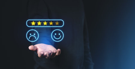 Hand holding glowing five-star rating with happy and sad smiley icons on dark background, representing online customer feedback and satisfactionの写真素材