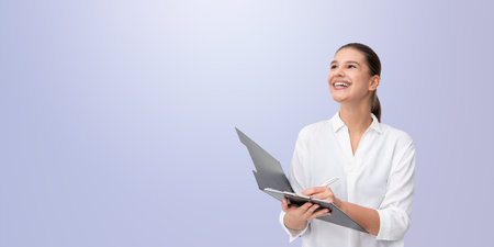 Woman holding folder and pen, wearing white shirt, smiling, soft gradient background. Professional, confident, inspiring business conceptの写真素材