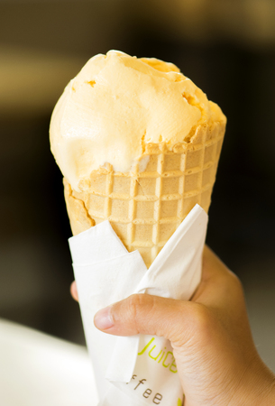 Hand holding vanilla ice cream in waffle cone.の写真素材