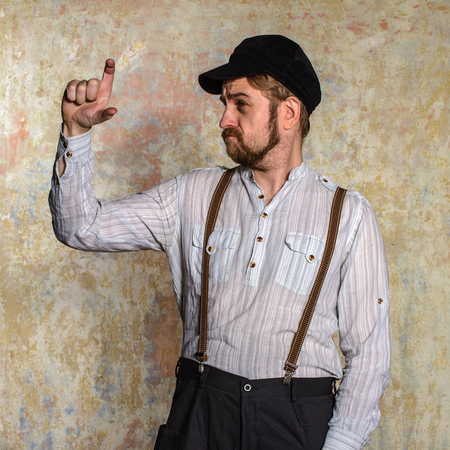 Portrait of handsome young man in white shirt and bow tie adjusting his suspenders and smiling at camera while standing isolated near old wallの写真素材