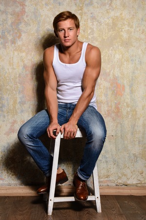stylish fashion man model sitting on the chair in jeans and a t-shirtの写真素材