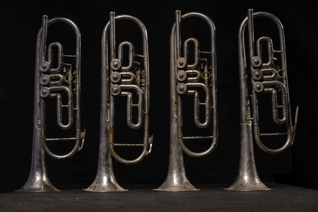 Four old brass wind instrument stand on a table on a black backgroundの写真素材