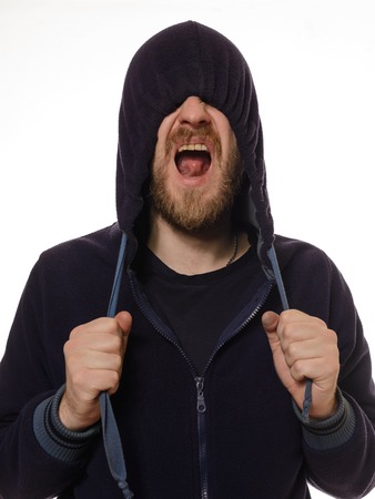 Unleashed emotions. Young man covering his face by blue hood and shouting while standing against white backgroundの写真素材