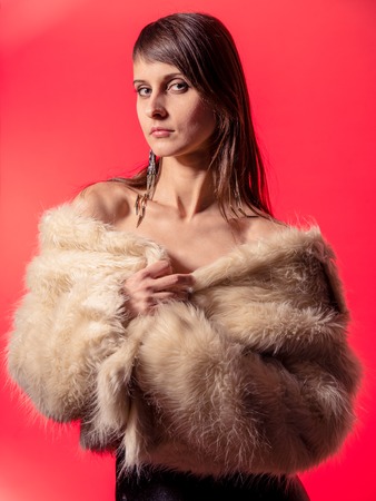 Young brunette lady in white fur coat posing on red backgroundの写真素材