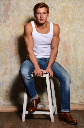 stylish fashion man model sitting on the chair in jeans and a t-shirtの写真素材