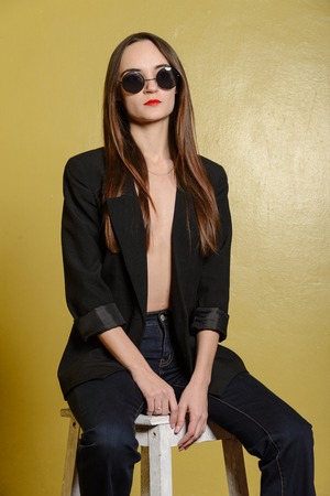 Fashion portrait of  girl with sunglasses  in jeans and a jacket sitting on chairの写真素材