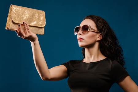 beautiful girl in a black dress with a golden clutch on blue backgroundの写真素材