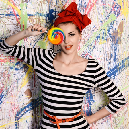 portrait of beautiful girl with big lollipop at wall with different color splashの写真素材